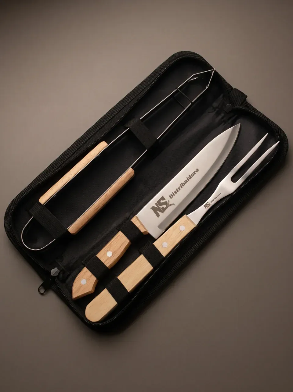Kit de três peças no estojo de nylon aberto: pegador, faca e garfo em aço inox com cabo de madeira, presos por alças elásticas.